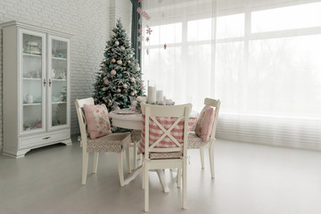 Beautiful Christmas decorated light living room with a Christmas tree, table and chairs. Concept of winter holidays and Happy New Year