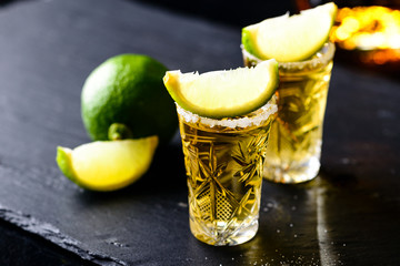 Gold Mexican tequila with lime and salt on dark table