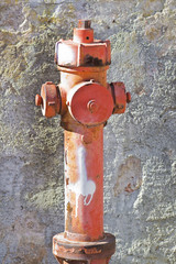 Old rusty red hydrant against a damaged plaster wall