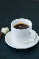 Cup of strong coffee and heart shaped dark and white chocolates on a black background.