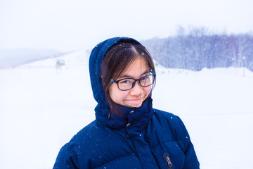 Happy asian female teenager in blue winter jacket standing outside in the snow smiling happily at camera