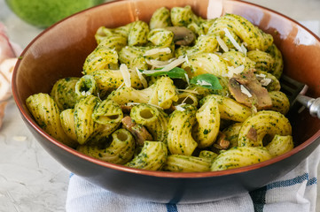 Cavatappi pasta with basil pesto and herbs in a plate on a white stone background.