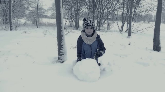 Small boy builds snowman. Family plays in snow. Yougster enjoys winter fun. Winter landscape with child and falling snow. Everything is covered with fresh powder. Winter background, Christmas theme