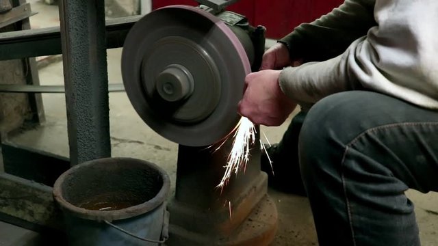 Man sharpening scissors at a whetstone in a grindery