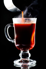 Process of preparing hot non-alcoholic mulled wine with orange and cinnamon on dark background