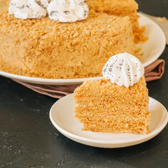 Honey cake with meringue decoration on top served on a white plate on a black backdrop.