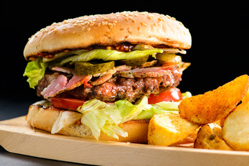 Tasty Gamburger with beef meat, tomato, pickes and potato wedges on wooden board