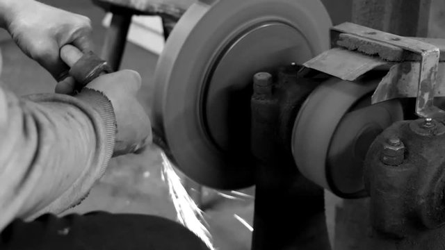 Man sharpening an axe at a whetstone in a grindery in black and white