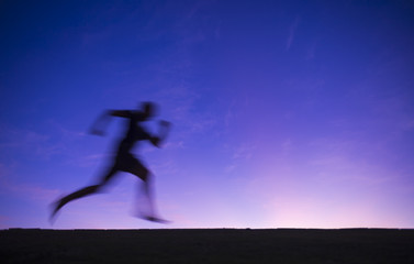 Silhouette blur of a runner passing across a purple twilight sunset sky background