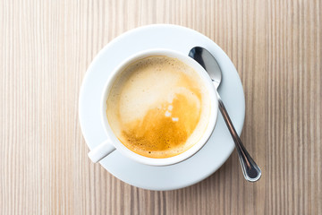 Latte coffee on the saucer with spoon in the wooden table, top view, flat lay