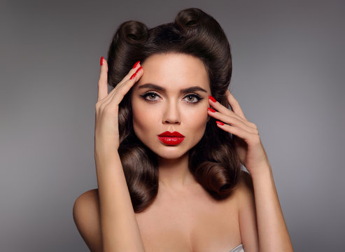 Pin up girl with red lips makeup, manicure nails and retro curls hair style. Retro woman looking at camera holds fingers near the head. High fashion photo. Sexy female portrait.