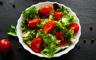 various fresh mix salad leaves with tomato in bowl on dark wooden background