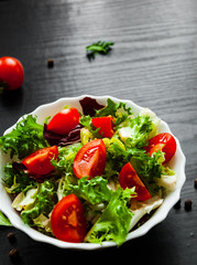 various fresh mix salad leaves with tomato in bowl on dark wooden background