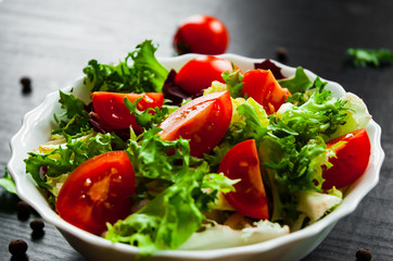 various fresh mix salad leaves with tomato in bowl on dark wooden background