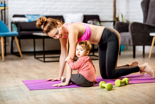 Young mother stretching on the mat with her baby son playing on the floor at home