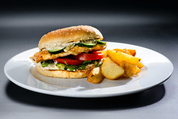 Tasty Gamburger with beef meat, tomato, pickes and potato wedges on a white plate