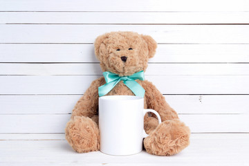 White coffee mug with plush bear on white wooden background.