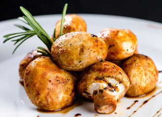 Delicious appetizing baked mushrooms with sauce in a white plate on dark background.