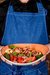 A man in a black shirt and a denim apron holds a dish © sapunovaphoto