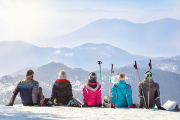 Skiers looking mountain hilles while sitting on snow, back view
