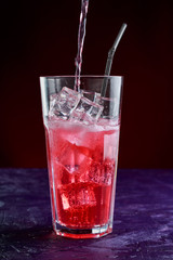 fizzy drink with ice in glass on dark background