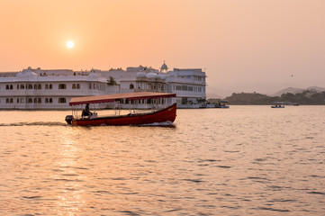 sunset over a boat and  the Lake Palace in Lake Pichola in Udaipur, Rajasthan