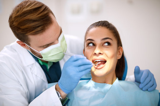 Dentist checking up girl’s teeth with mirror