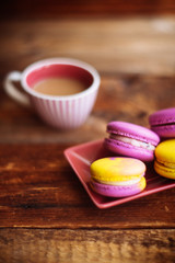 A cup of hot black coffee and bright macaroons on a wooden table at dark background with colorful bokeh