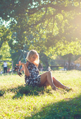 Portrait of fashionable young sensual blonde woman in garden sitting on the grass.