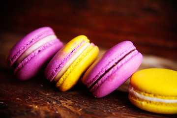 Colored macaroons pastel colors with different flavors on glass plate with paper towel. Bright and delicious dessert/ Wooden background