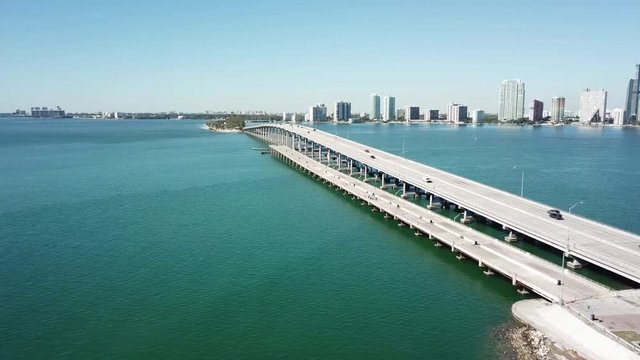 Stunning 4k aerial drone panorama shot of highway road on huge steel modern bridge across turquoise blue ocean cityscape