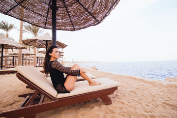 Beautiful young woman with sexy legs and body getting a sun-tan lying on a deck-chair on the sea beach. Summer vocation.