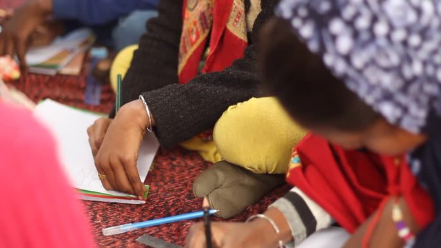 Girl in Indian village school studies with other kids. Wearing patterned scarf. Tilt up from books to her face. Narrow depth of field. Winter. Bengal, India.