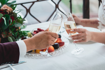 Glasses with champagne drink in bride and groom hands. Happy newlyweds drinking. Loving couple created new family.