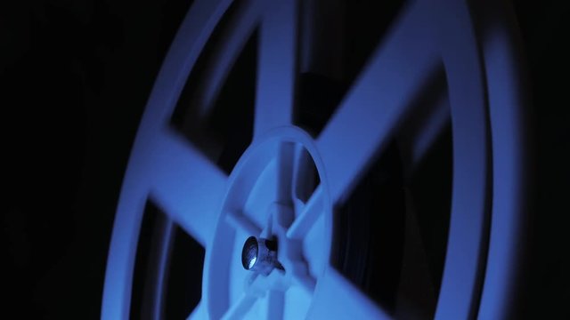 Old 8mm film projector playing in the night in dark room with blue light. Rotation reel with tape on the video, audio tape recorder or player. Close-up of a reel with a film. 4k.