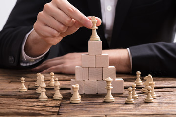 Businessperson Placing King Chess Piece On Top Of Wooden Blocks