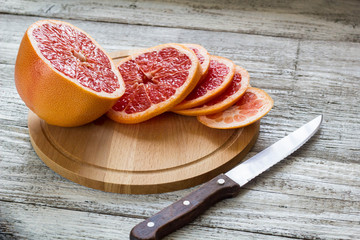 Sliced pieces of grapefruit with a knife. On white wooden background