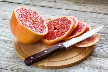 Sliced pieces of grapefruit with a knife. On white wooden background