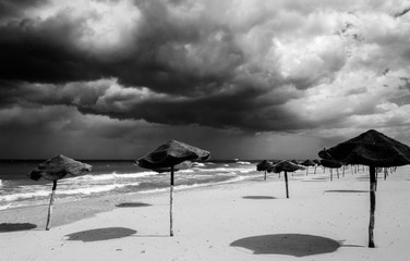 Bedrohliche Wolken am Strand mit Sonnenschirmen monochrom