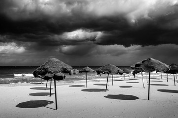 Bedrohliche Wolken am Strand mit Sonnenschirmen monochrom