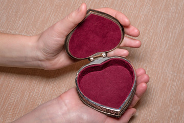 Opened old vintage silver heart-shaped casket in female hands on light coloured background.
