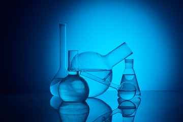 different glass flasks on reflecting table in laboratory on blue