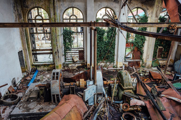 Ruined abandoned electrical substation. Rusty generator at machinery. Demolished roof