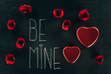 lettering BE MINE surrounded with rose petals and heart boxes on black surface, st valentines day concept
