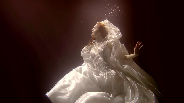 Wonderful woman is posing dressed in lovely wedding dress underwater