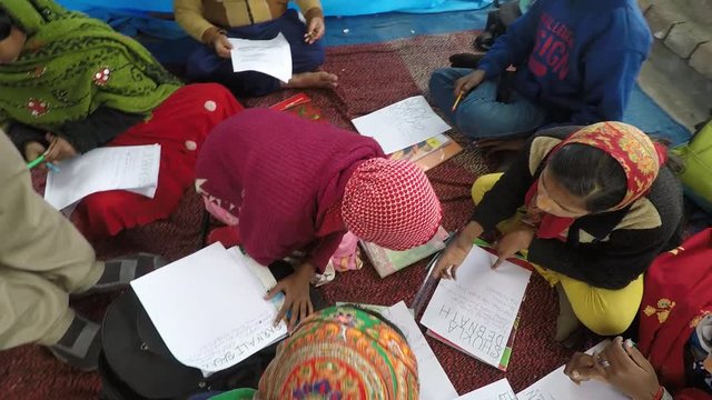 Boys and girls in an Indian village school sit together and write on papers. Crane shot looking down at circle of kids from above the descending to equal level. 60 fps. Bengal, India