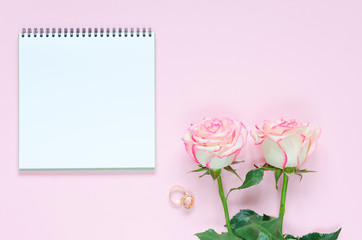 Two pink blooming fresh rose flower with notepad on pink background