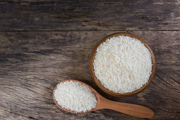 top view of raw dry Thai jasmine rice seeds in a bowl on old and crack wooden board with copy space for text.
