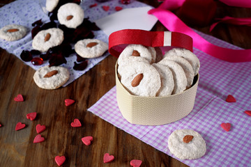 White cookies with almond in a heart-shaped box. Tiny hearts are scattered around. Treats for Valentine's Day