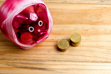 SAVING  DETERIORATE CONCEPT. Red piggy bank with bandage and small stack of coins on the wooden table over white background.